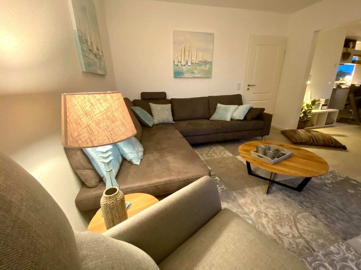 A living room with a sofa, a coffee table, and a lamp. There is a painting on the wall and a door leading to another room.