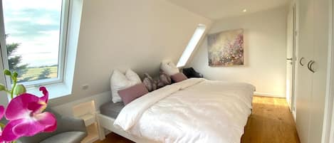 Un dormitorio con una cama, una silla, un ventanal y un cuadro.