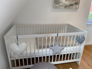 En vit spjälsäng med hjärtformade kuddar och en stickad matta.