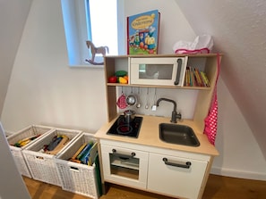 Ett lek-kök för barn med ett fönster, en bok på hyllan och förvaringskorgar.