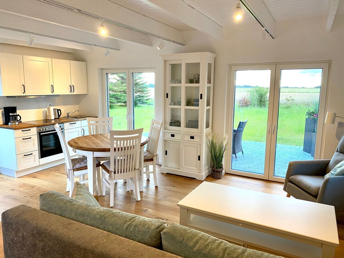 A modern kitchen with white cabinets, a dining table with chairs, a built-in cabinet with glass doors, and a sliding glass door leading to a patio with outdoor furniture.
