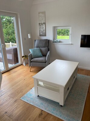 Ett rum med ett vitt bord, en grå fåtölj, ett fönster med utsikt och en väggmonterad TV.