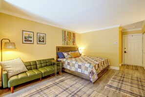 A bedroom with a green sofa, a bed with a quilt, two framed pictures on the wall, and a door. - Lake Lure Mtn Getaway w/ Private Balcony (Lake Lure)