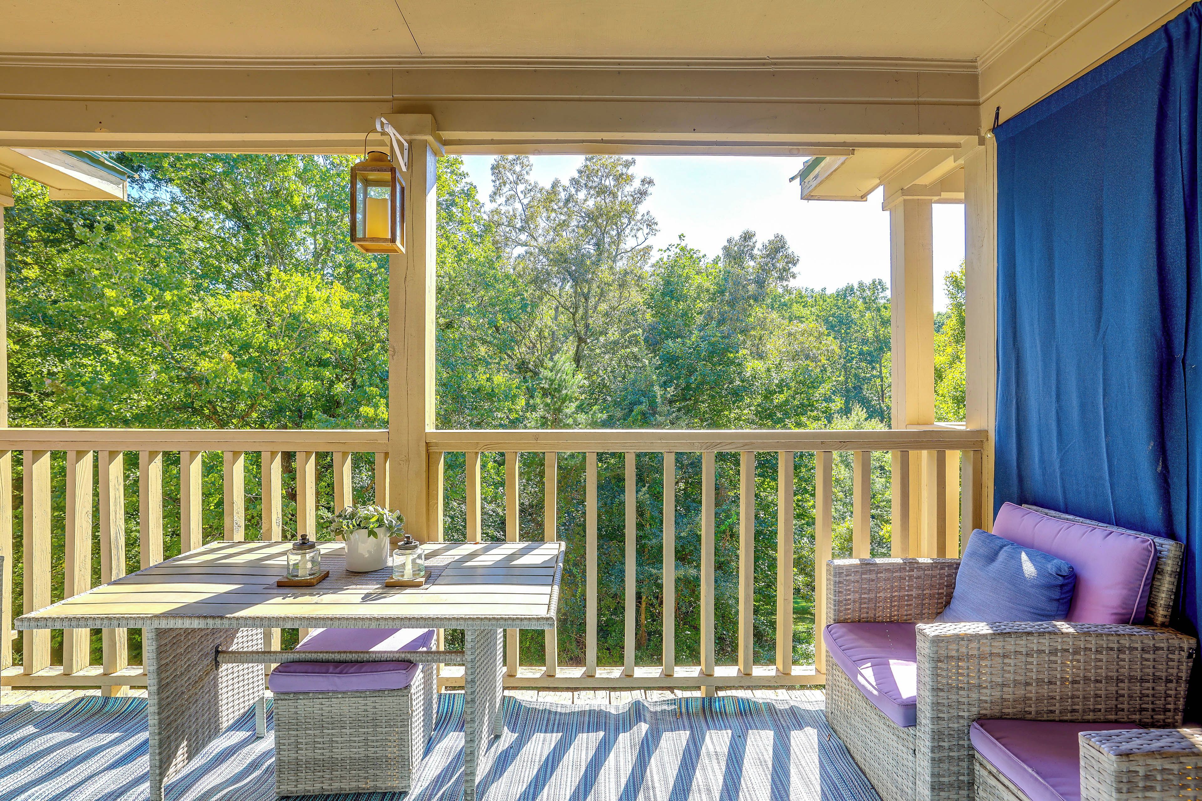 A covered outdoor seating area with a table and chairs, a lantern, and a view of trees.