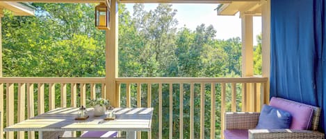 A covered outdoor seating area with a table and chairs, a lantern, and a view of trees.