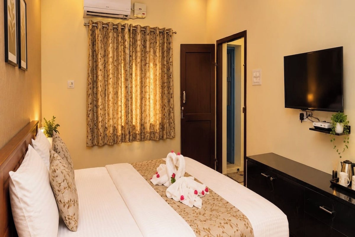 Una habitación de hotel con cama, televisión de pantalla plana, cómoda y ventilador de techo.