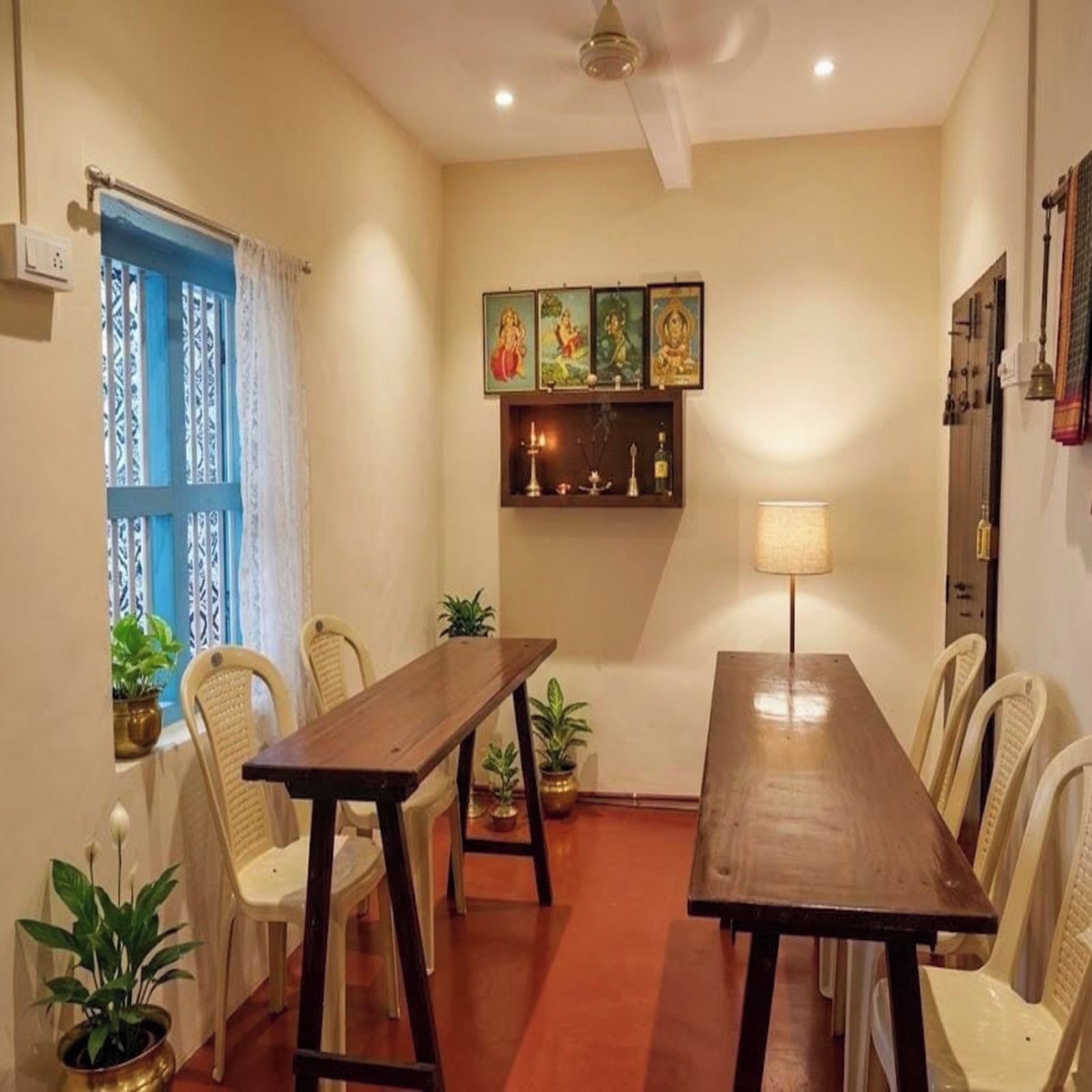 Un comedor con mesa y sillas de madera, ventilador de techo y pared decorada con cuadros religiosos.