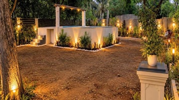 A well-lit outdoor area with a stone structure, steps leading to a covered area, and surrounding greenery.