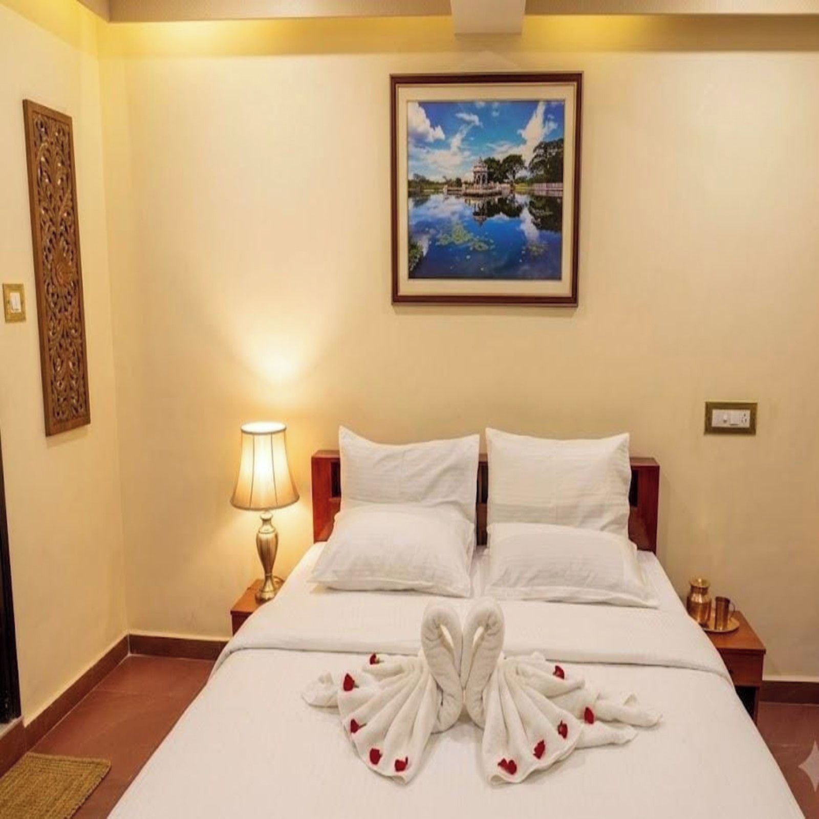 Una habitación de hotel con cama, mesita de noche, lámpara, un cuadro en la pared y un adorno decorativo.