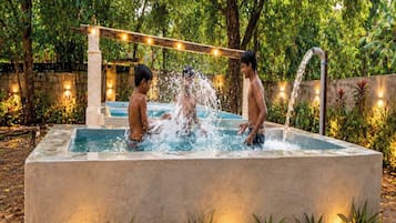 Piscina rectangular con borde de piedra, rodeada de plantas y una guirnalda de luces.