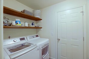 Un espace buanderie équipé d’un lave-linge et d’un sèche-linge à chargement frontal, avec des étagères au-dessus pour ranger les produits de nettoyage, et une porte blanche.