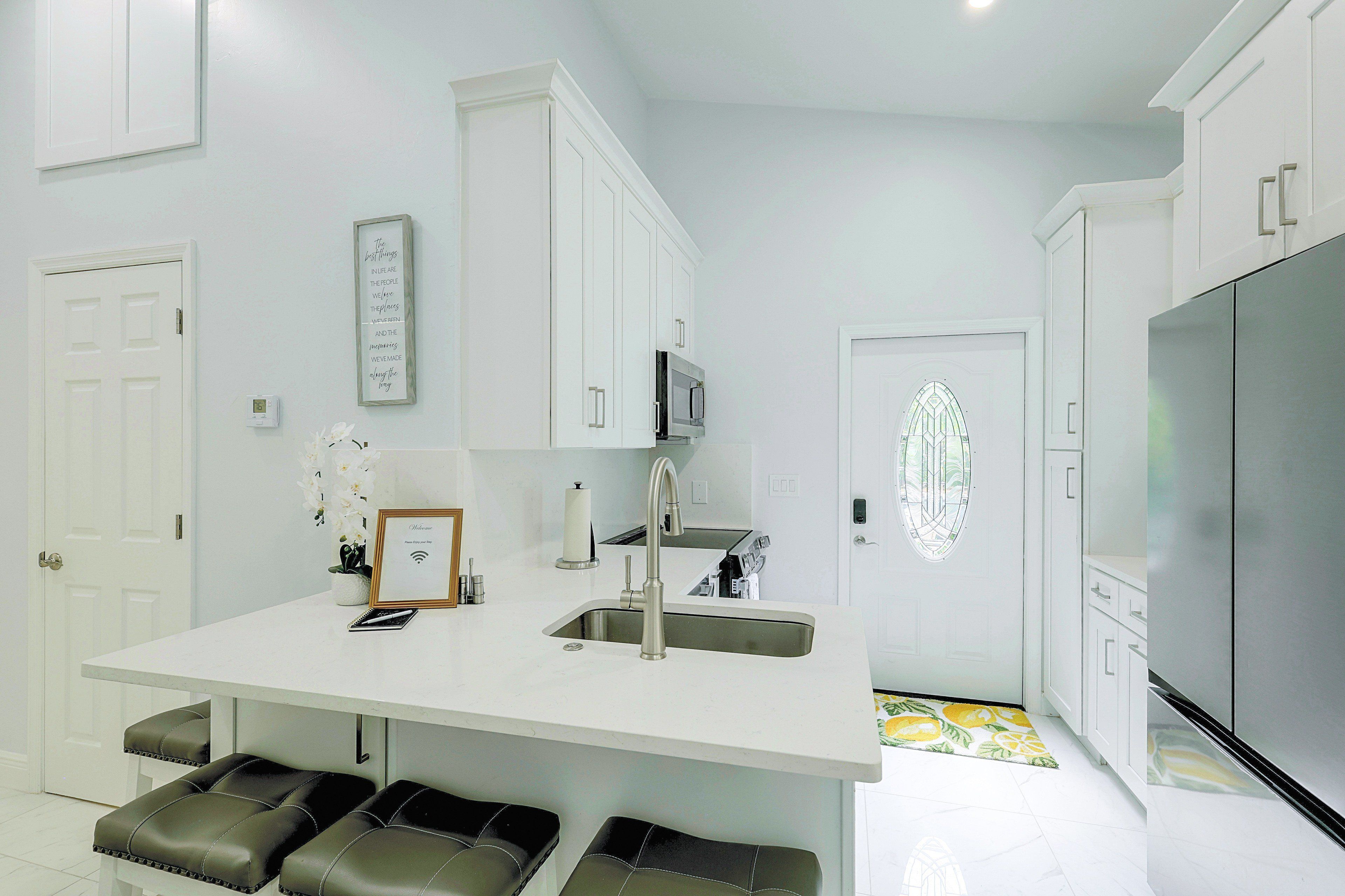 A modern kitchen with white cabinetry, a stainless steel refrigerator, a built-in microwave, and a bar area with stools.