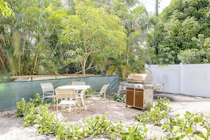 Eine Terrasse mit Grill, Stühlen und Tisch, umgeben von viel Grün.