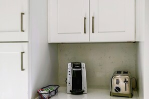 A kitchenette with white cabinets, a Keurig coffee maker, a toaster, and a basket of coffee pods. - Naples Guest House Near Beaches & Downtown! (Naples)