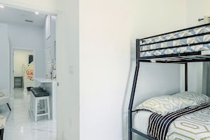 Ein Zimmer mit Etagenbett, einem weißen Schreibtisch und einem Stuhl. Im Hintergrund ist ein Badezimmer zu sehen.