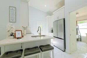 A modern kitchen with white cabinetry, a stainless steel refrigerator, and a bar area with stools. - Naples Guest House Near Beaches & Downtown! (Naples)