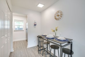 Een moderne keuken met een eethoek, met een kookeiland en barkrukken, een wandklok en een raam met zonwering.