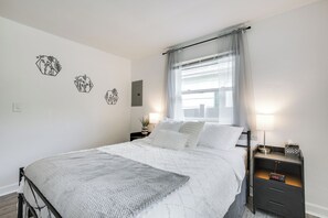 A neatly made bed with a white duvet and a gray throw blanket, a bedside table with a lamp, and a wall clock. - 2-Condo Hub! 1/2 Mi to University of Dayton (Dayton)