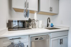 A modern kitchen with white cabinetry, a stainless steel microwave, a dishwasher, and a sink with a faucet.