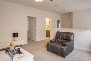 A living room with a leather sofa, a coffee table with books, a lamp, and a door leading to another room. - Yard, Patio, Office! Spacious Home in Union Park (Little Elm)