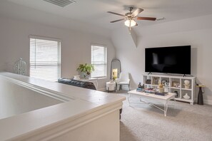 A modern living room with a large flat-screen TV, a ceiling fan, and a white console table with decorative items. - Yard, Patio, Office! Spacious Home in Union Park (Little Elm)