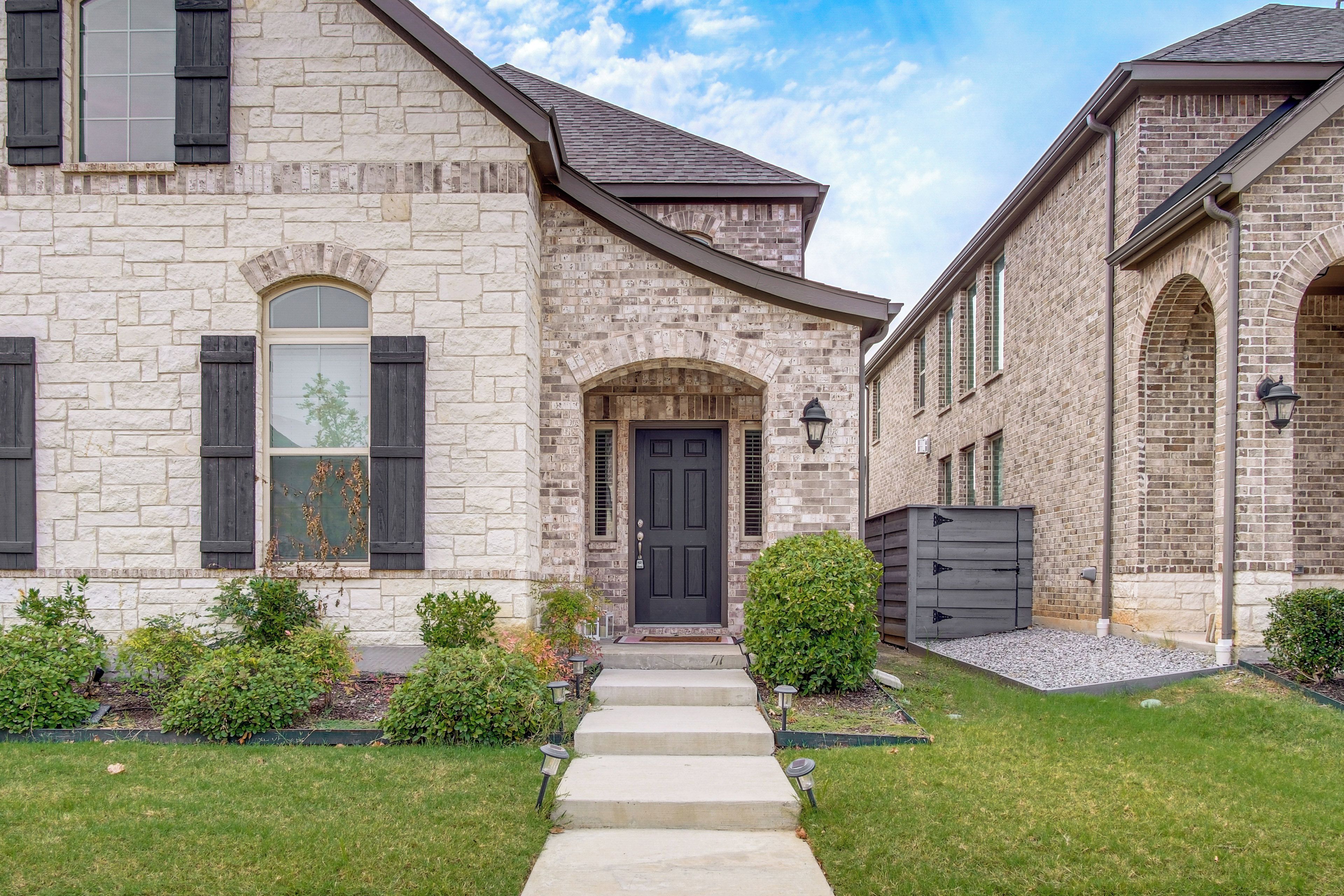 A two-story stone house with a front entrance, a covered porch, and a small garden.