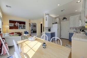 Ein helles, offenes Wohn- und Esszimmer mit einem Holztisch, weißen Stühlen und einer Küche mit weißen Schränken.