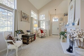 A spacious room with a large window, a white armchair, a floral sofa, a vintage trunk, and a fireplace with decorative items. - San Jose Furnished Stay w/ Laundry (San Jose)