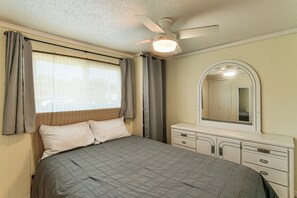 Een slaapkamer met een bed, een dressoir, een plafondventilator en een raam met gordijnen.