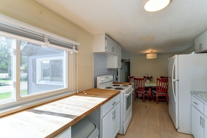 A compact kitchen with a window, a stove, and a refrigerator. - Steps to Bay! Home w/ Hot Tub in Tawas City (Tawas City)