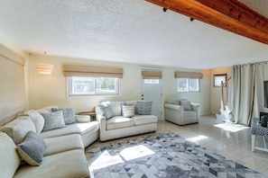 A spacious living room with a large sofa set, a patterned rug, and a wooden ceiling beam. - Steps to Bay! Home w/ Hot Tub in Tawas City (Tawas City)