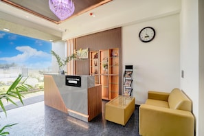 A reception area with a reception desk, a clock, a sofa, and a wall with shelves. - Classic Hotel Nishara (Mysore)
