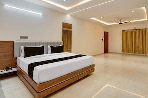 A modern hotel room with a large bed, a bedside table, a telephone, and a ceiling fan. - Classic Hotel Nishara (Mysore)