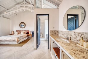 Ein Schlafzimmer mit einem großen Bett, einem Nachttisch, einem Spiegel und einer Tür zu einem Badezimmer mit Waschbecken und Spiegel.