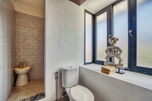 Une salle de bain moderne équipée de toilettes, d’un bidet et d’une fenêtre agrémentée d’une sculpture décorative.
