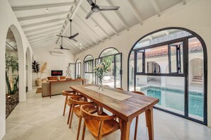 Un vaste espace de vie comprenant une table à manger en bois, des sièges confortables et de grandes fenêtres donnant sur une piscine.
