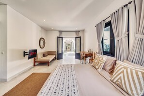 Ein modernes Hotelzimmer mit Bett, einer Couch, einem an der Wand montierten Fernseher und Blick ins Freie durch das Fenster.