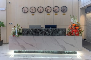 A reception desk with a marble top, multiple clocks on the wall, and a floral arrangement on the right.