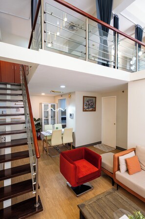 A modern apartment with a staircase, a dining area, a red sofa, and a living room with a beige sofa. - Forbestown BGC |Luxury 2BR loft| Pool & Gym Use (Taguig)