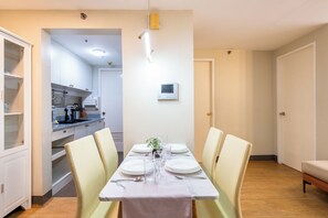 A dining area with a table set for four, a kitchen in the background, and a thermostat on the wall. - Forbestown BGC |Luxury 2BR loft| Pool & Gym Use (Taguig)