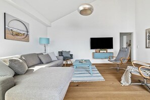 A modern living room with a sectional sofa, a television, and a blue accent wall. - Apartment in Olpenitz with swimming pool (Olpenitz)