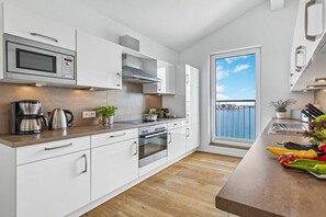 A modern kitchen with white cabinetry, stainless steel appliances, and a wooden countertop. - Apartment in Olpenitz with swimming pool (Olpenitz)