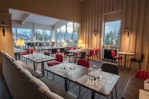 A restaurant with multiple tables and chairs, large windows offering a view of the mountains, and a cozy interior with warm lighting.