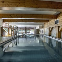 A swimming pool with clear water, wooden beams, and a stone wall.