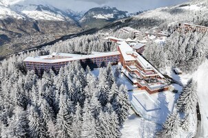 Un resort cubierto de nieve con varios edificios, rodeado de bosques densos y montañas al fondo.