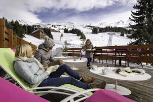 Un groupe de personnes assises sur des meubles de jardin, avec une montagne enneigée en arrière-plan.