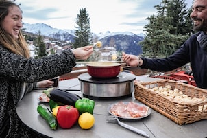 A dining table with a pot of soup, vegetables, bread, and meat.