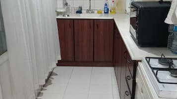 Une cuisine compacte avec des meubles en bois, un plan de travail blanc, une cuisinière à gaz et un tapis à motifs.
