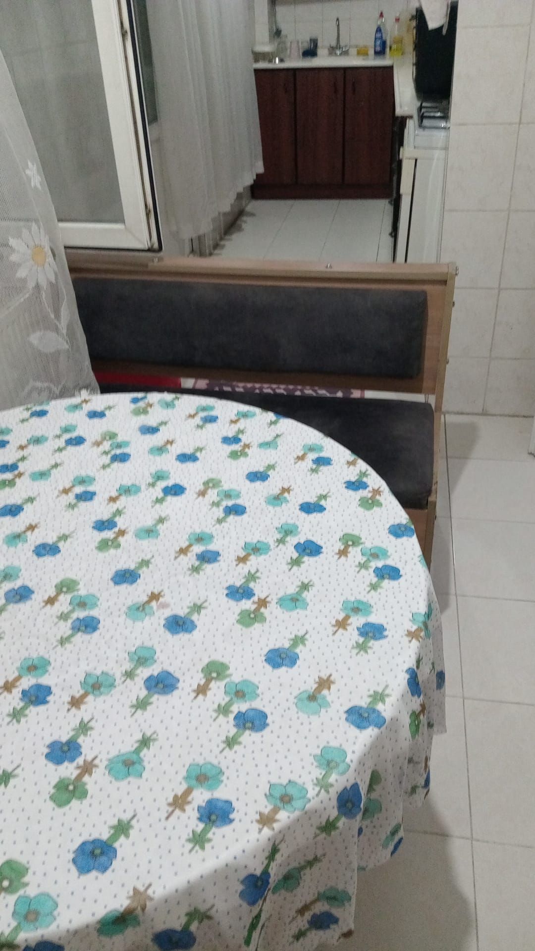 Een ronde tafel met een tafelkleed met bloemenprint, een bank en een keuken op de achtergrond.