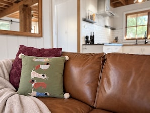 A brown leather sofa with a green pillow featuring dog illustrations. - Resort-style Executive and Family Retreat (Hornsby)